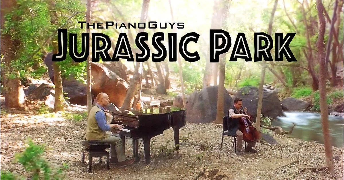 The Piano Guys perform "Jurassic Park" in a forest setting with a grand piano and cello.