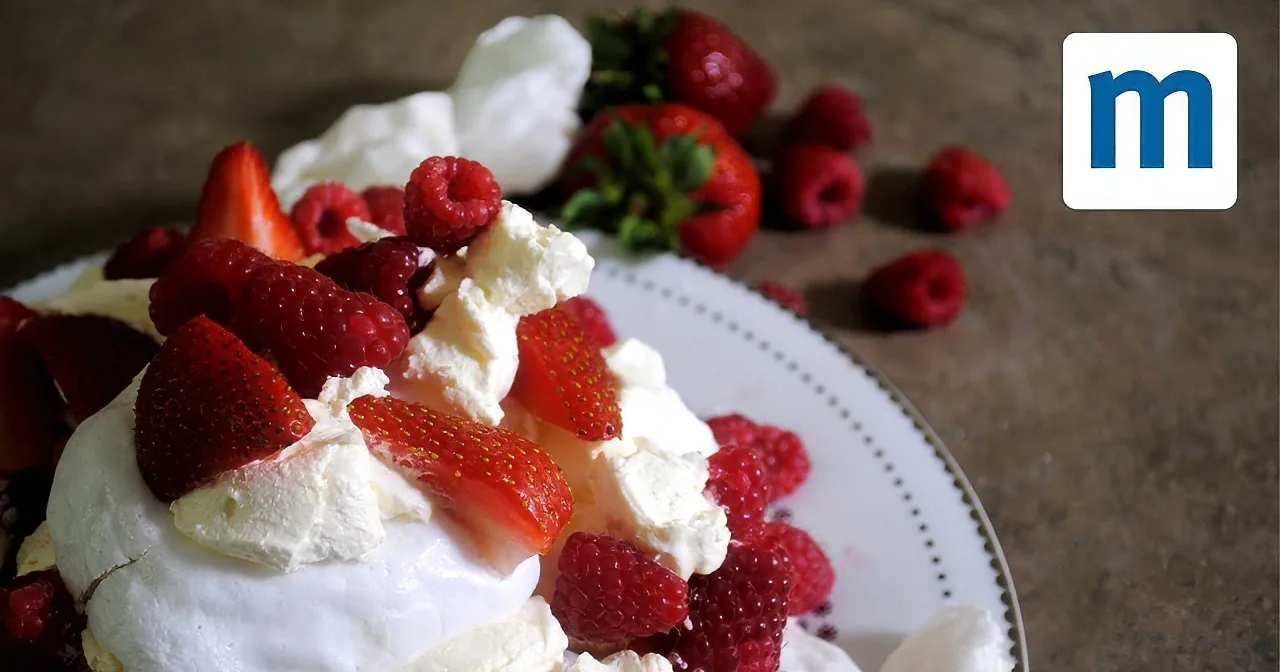A dessert with meringue, whipped cream, strawberries, and raspberries on a white plate.