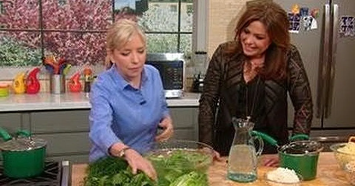 Two women in a kitchen preparing food, one in blue shirt arranging greens, another in black jacket assisting.