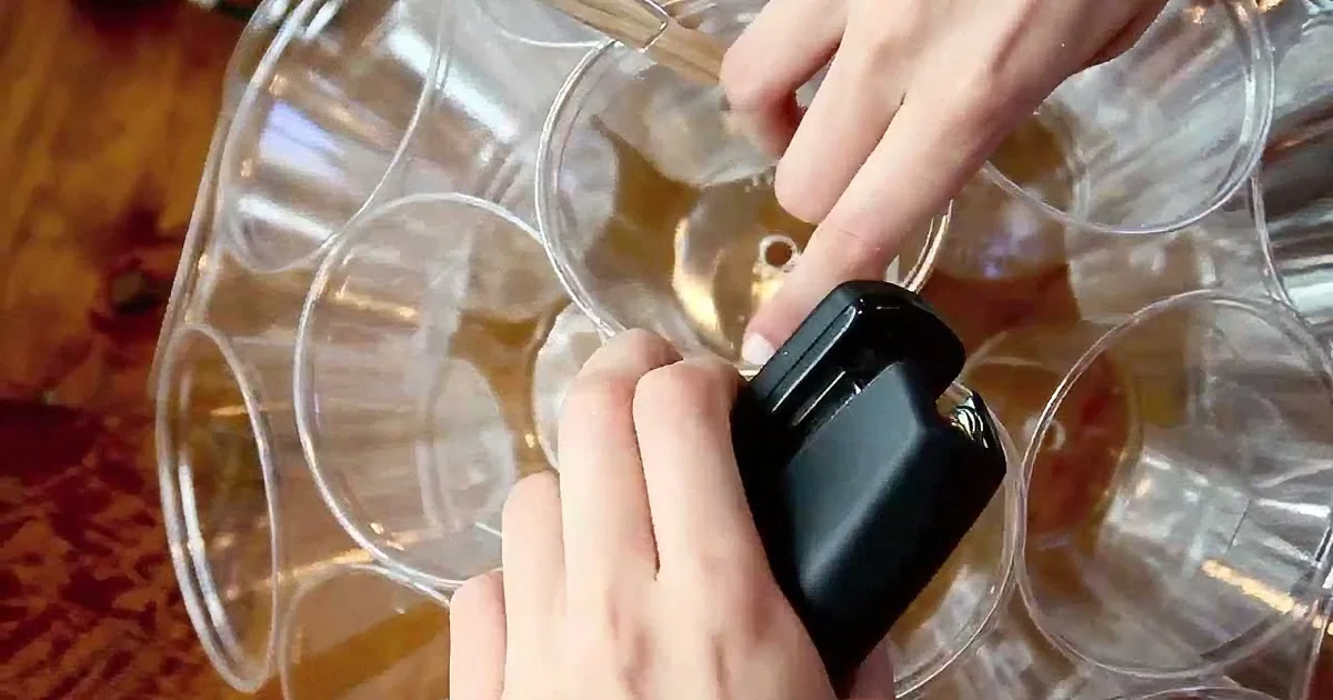 A person is using a black tool to remove a small object from a clear plastic container.