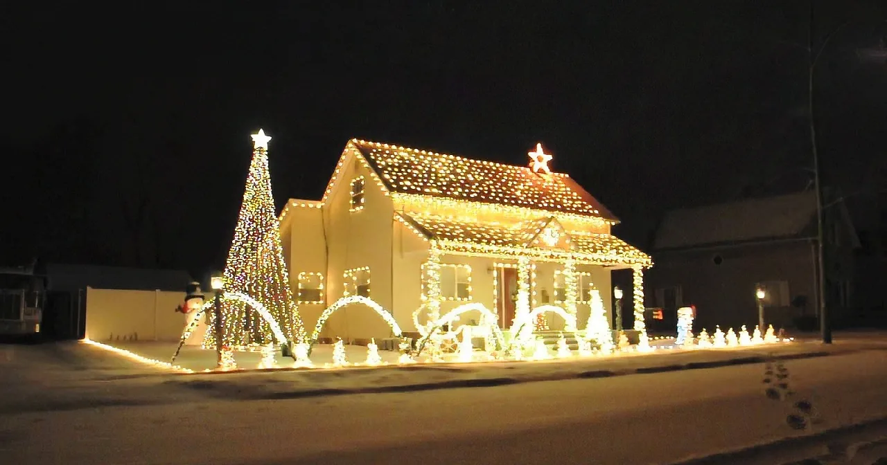 A house adorned with festive Christmas lights and decorations stands illuminated against a dark night sky.