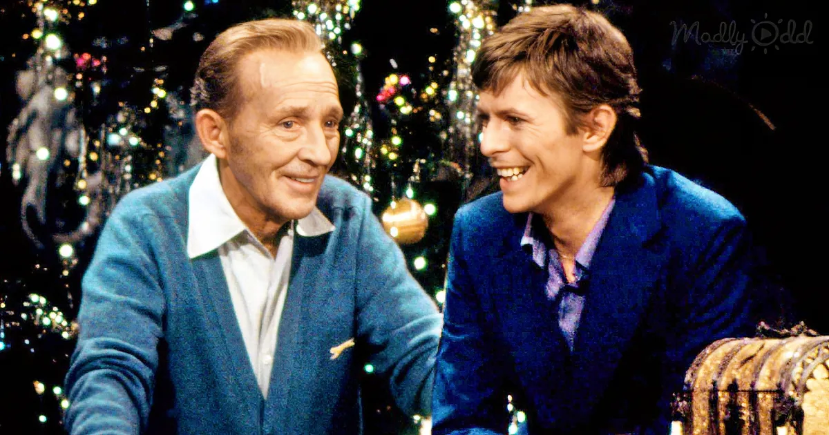 Two men in blue attire share a laugh, decorated Christmas tree in the background.