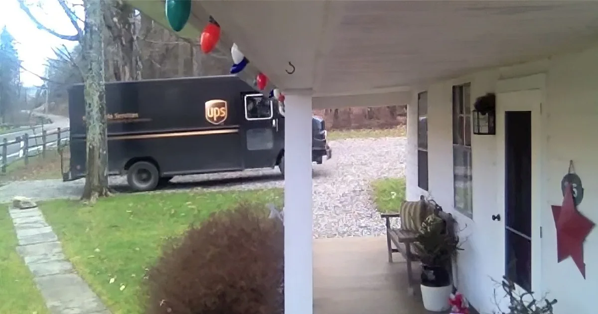 A UPS delivery truck is parked outside a house with a porch decorated for Christmas.