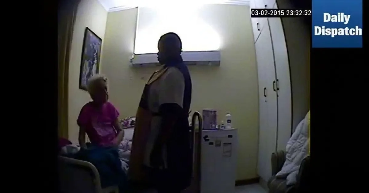 A man stands near a seated woman in a dimly lit room with medical equipment and a clock showing 23:32:32.