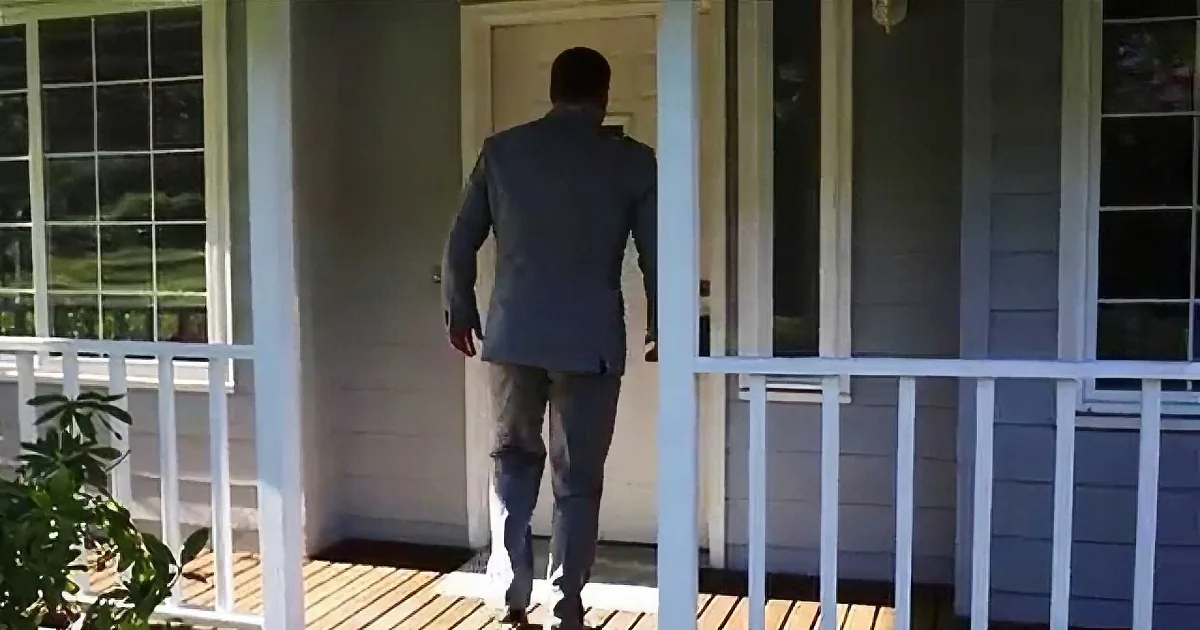 A man in a suit walks down a porch towards a door.