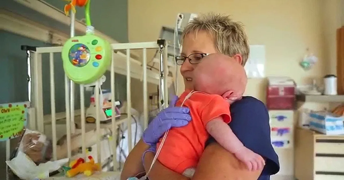 A woman holds a baby in a hospital room, surrounded by medical equipment and toys.