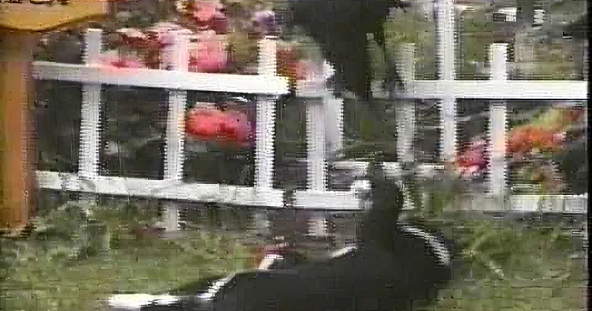 A person in a black outfit is climbing over a white picket fence with flowers behind it.