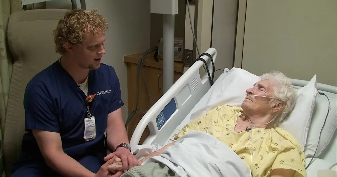 A nurse comforts an elderly patient in a hospital bed, holding her hand.