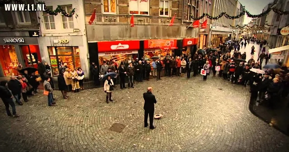 A man in black pants and a white shirt is performing on a cobblestone street surrounded by a crowd.