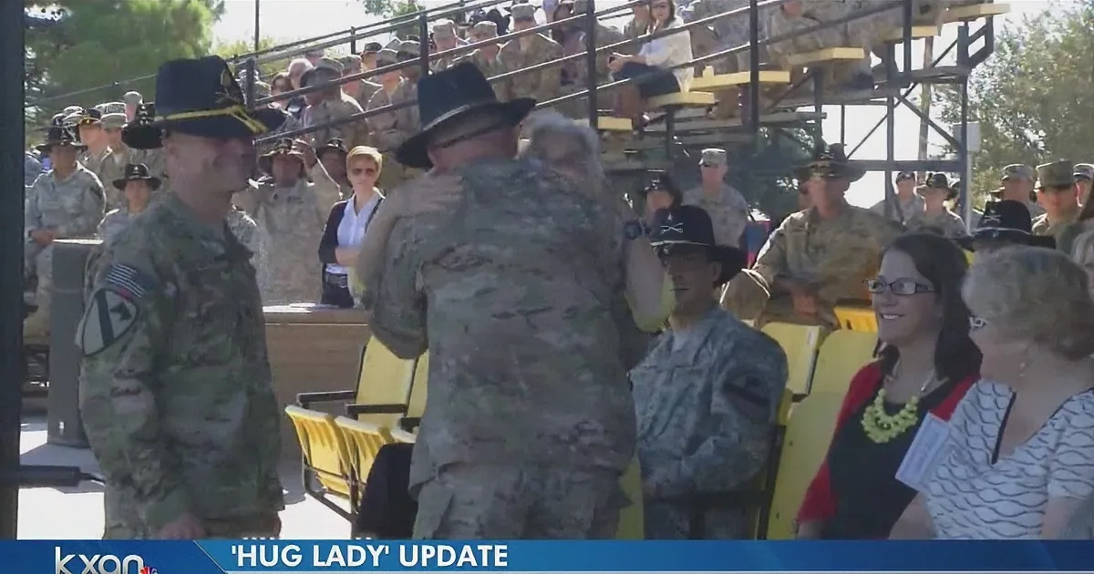 A soldier in uniform hugs a woman in civilian attire at a military event.