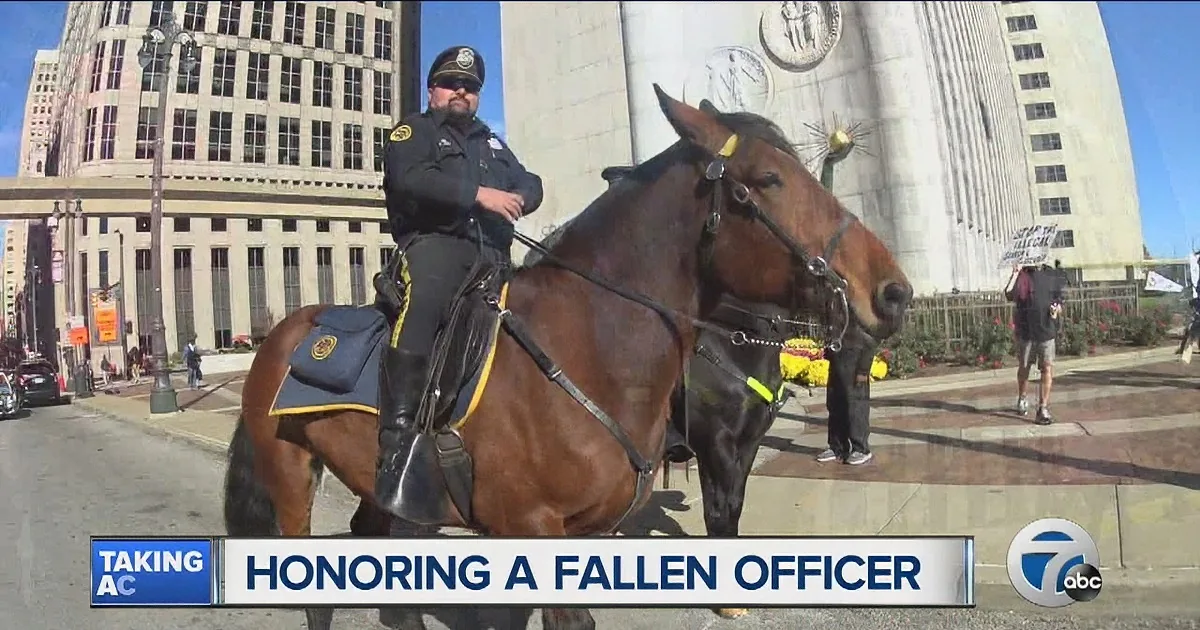 A police officer on horseback stands in front of a large building, honoring a fallen officer.