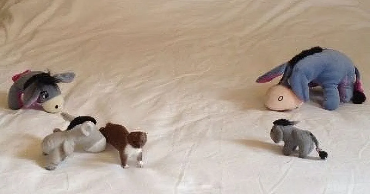 Stuffed animals, including a donkey, a horse, and a unicorn, are arranged on a white surface.