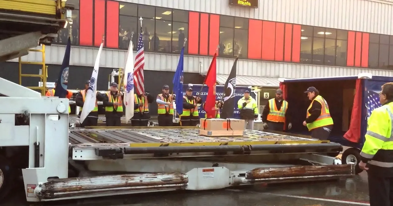 Workers in safety vests stand with flags near a large piece of equipment at an airport.