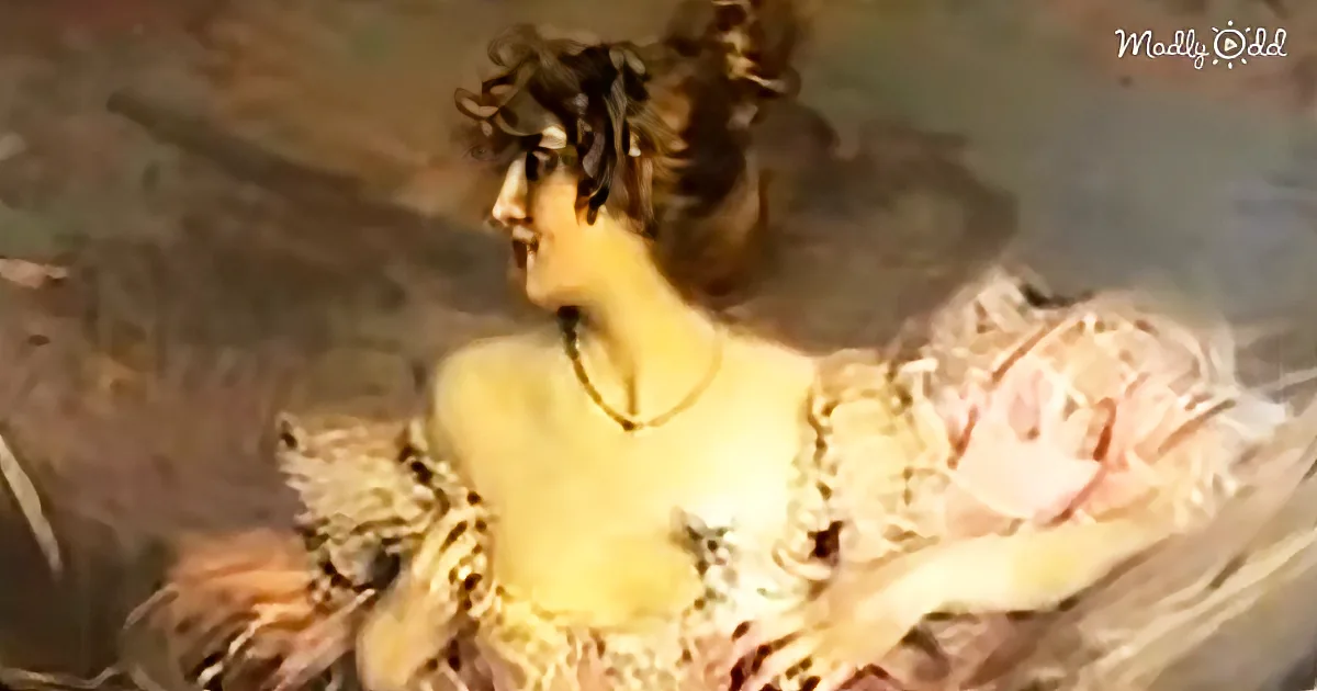 A woman in a vintage dress with a necklace, sitting with her back turned, in a dimly lit setting.