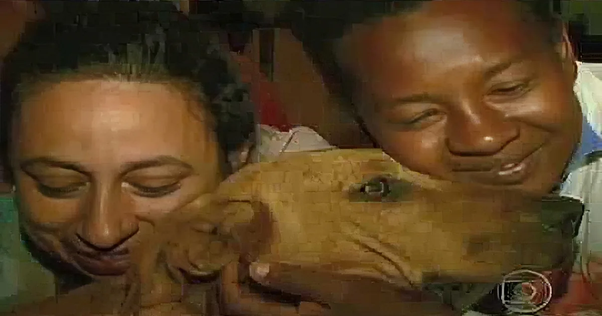 A smiling couple holds a small, light-brown dog, with the dog's head resting on the woman's shoulder.