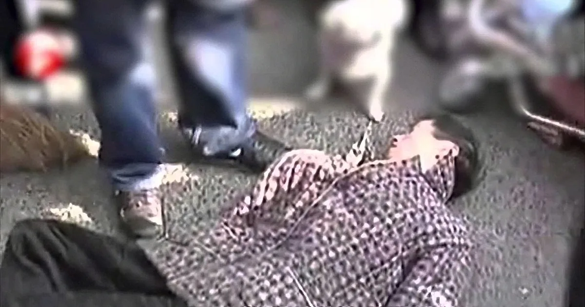 A person in black boots stands over a person lying on the ground, appearing injured or unconscious.
