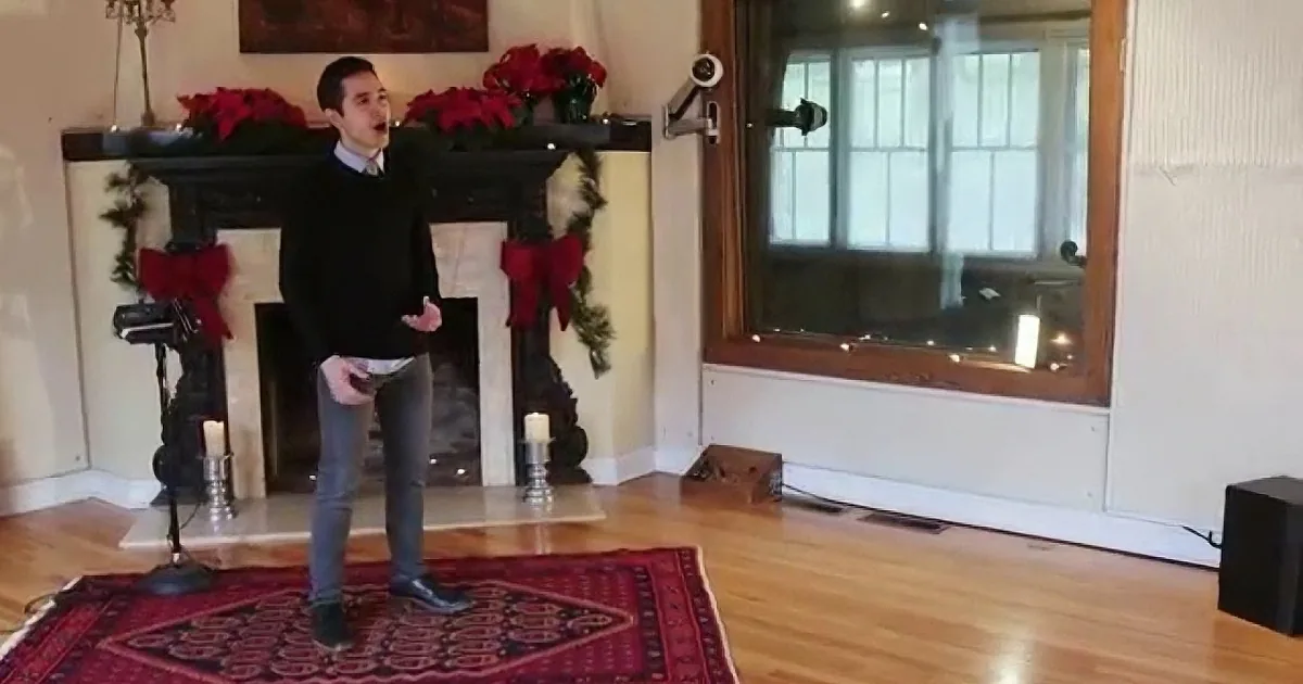 A man stands in a festive living room with a fireplace, red decorations, and a wooden floor.