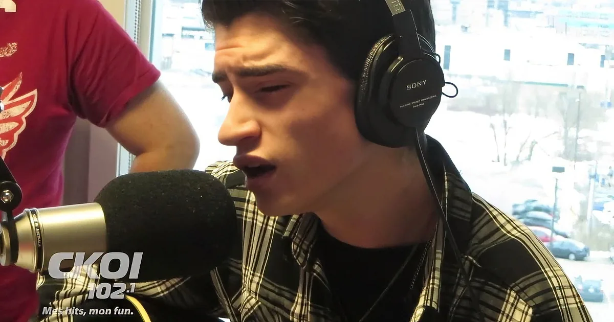 A person wearing headphones sings into a microphone in a radio studio.