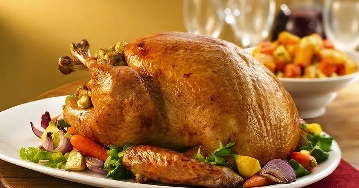 A roasted turkey with stuffing and vegetables on a festive table setting.