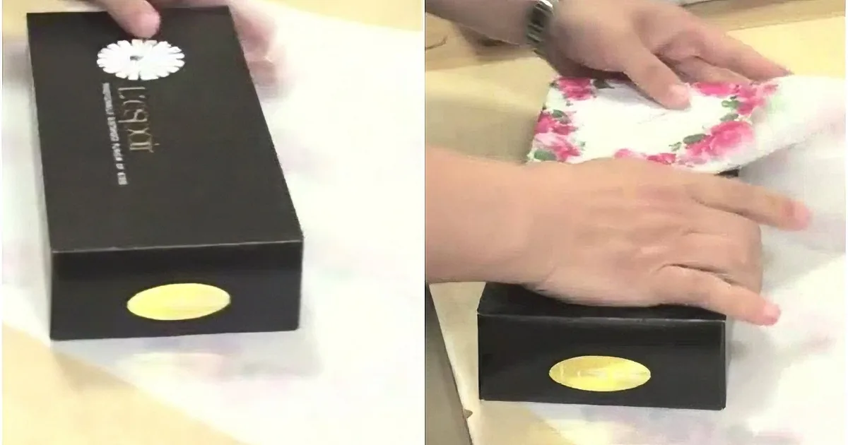Hands open a black box with a white flower logo, revealing a floral-patterned item inside.