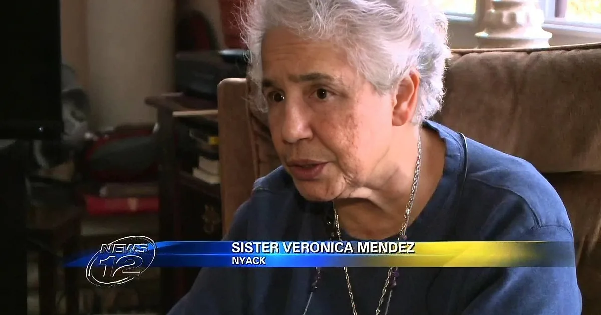An elderly woman with white hair, wearing a blue shirt, is speaking on a news segment.
