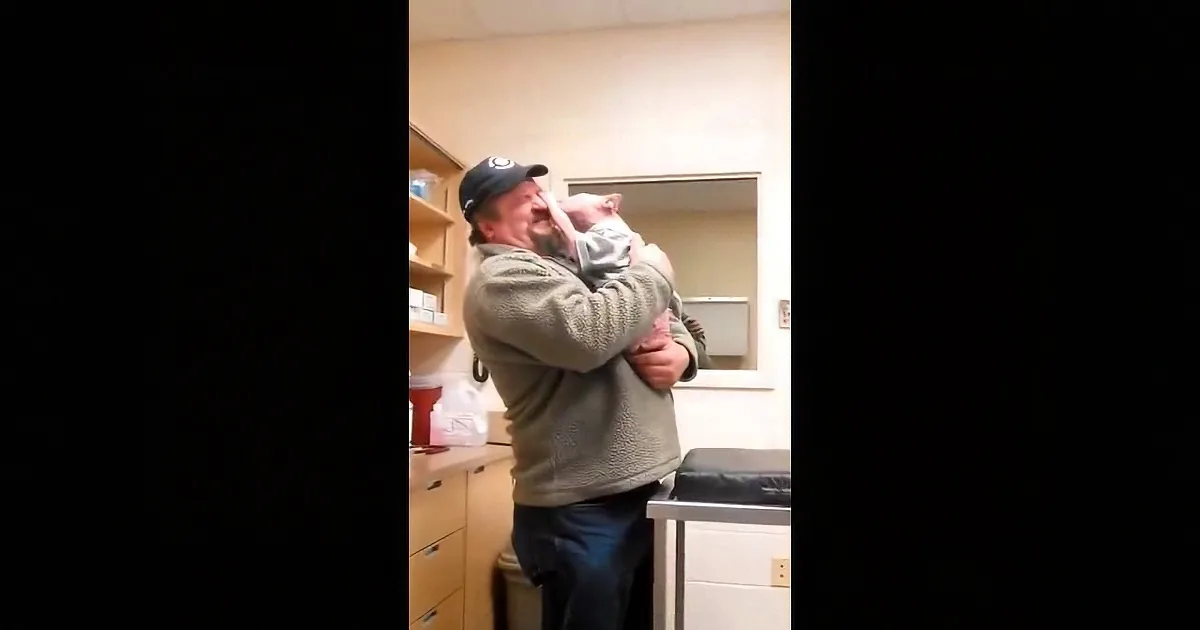 A man in a cap holds a baby in a kitchen, both looking up.