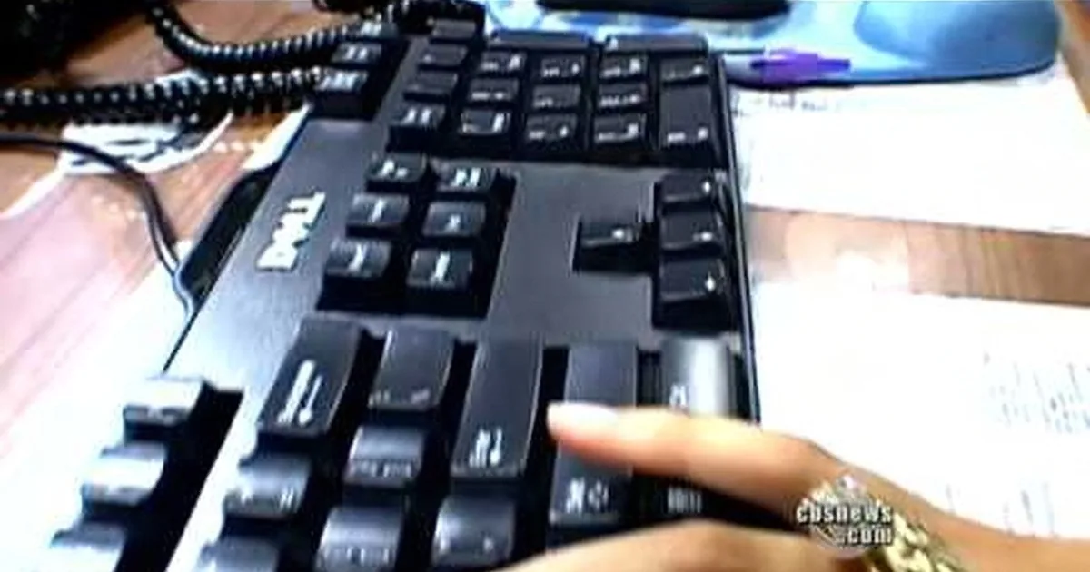 A Dell keyboard is shown with a hand interacting with it, placed on a desk with a phone and papers nearby.