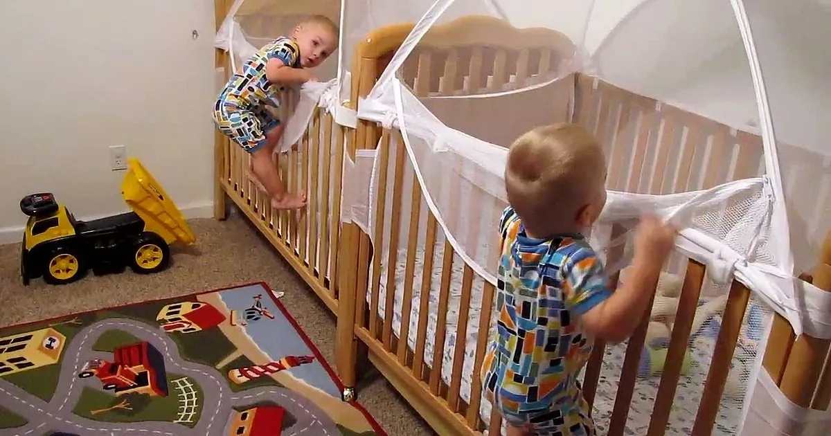 Two toddlers in colorful pajamas climb out of cribs in a room with a toy truck and a play mat.