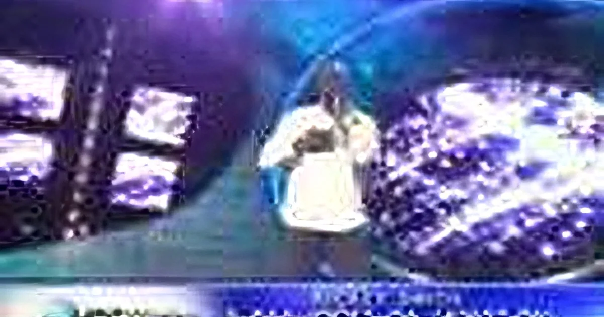 A person in a white outfit stands on a stage with a large screen displaying a blue and white background.