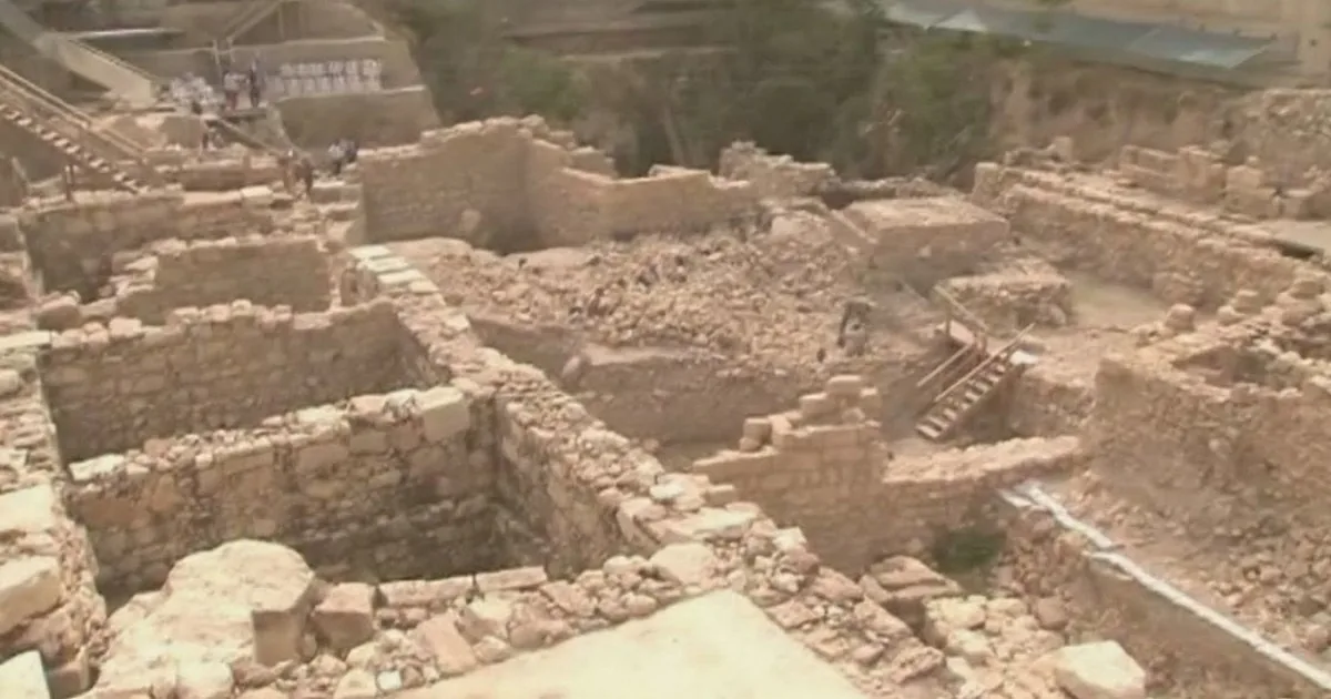 Ancient stone ruins with stairs and walls, possibly archaeological site, with people in the background.