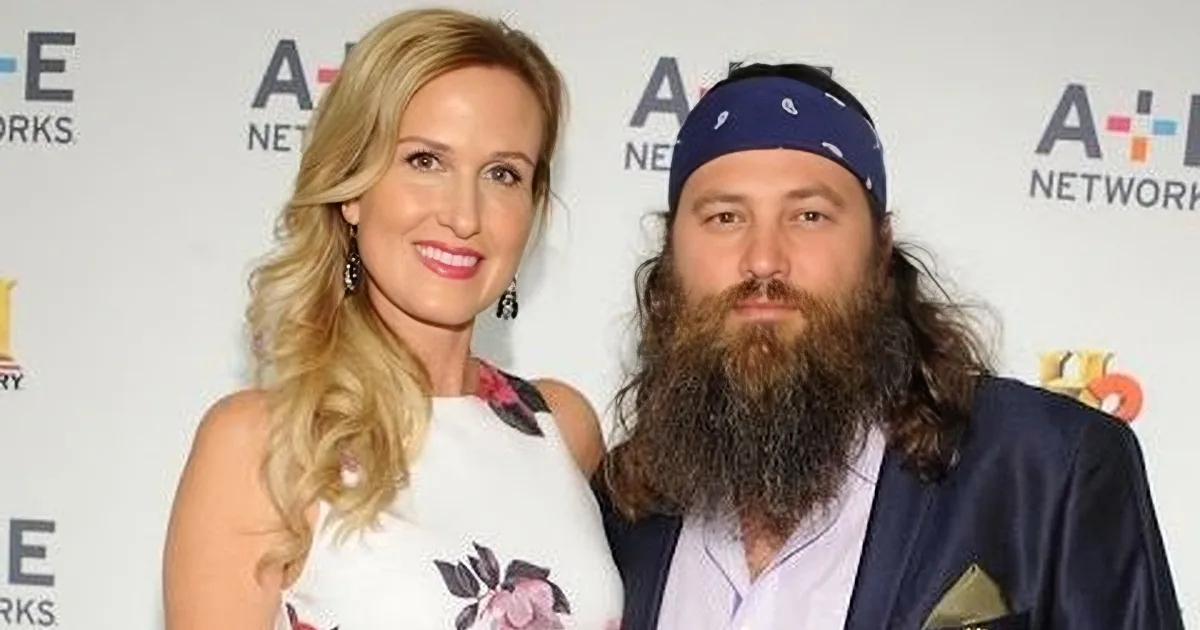 A blonde woman in a floral dress stands next to a man with a long beard and bandana, both smiling at the camera.