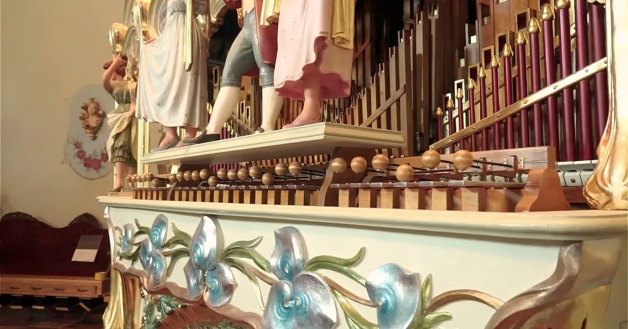 An ornate organ with colorful floral decorations and golden accents is shown, featuring a row of pipes and intricate details.