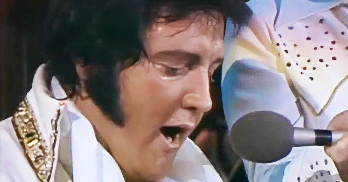 Elvis Presley in a white suit with a microphone, singing passionately.
