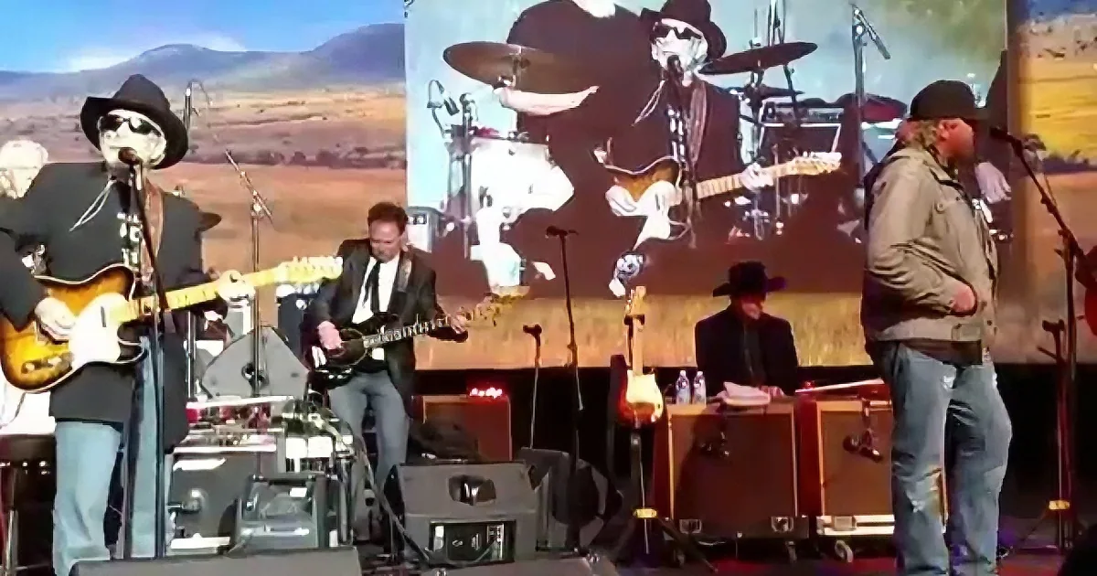 A band performs on stage with a large screen displaying a similar image of the same band.