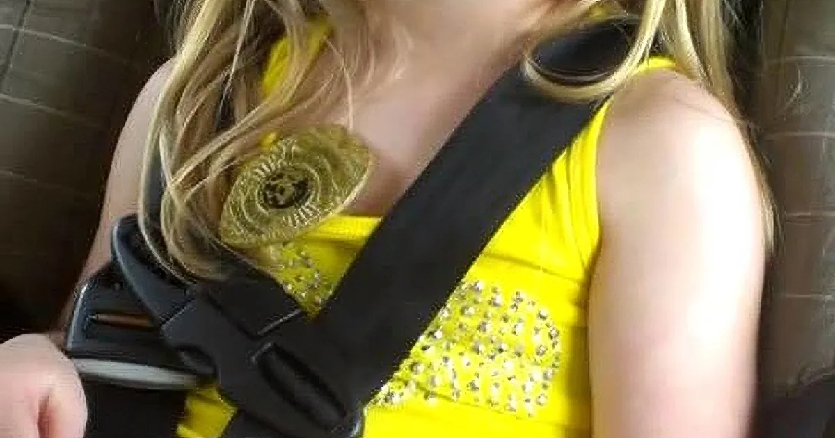 A person in a yellow dress with a black strap across their chest, possibly a seatbelt or harness.