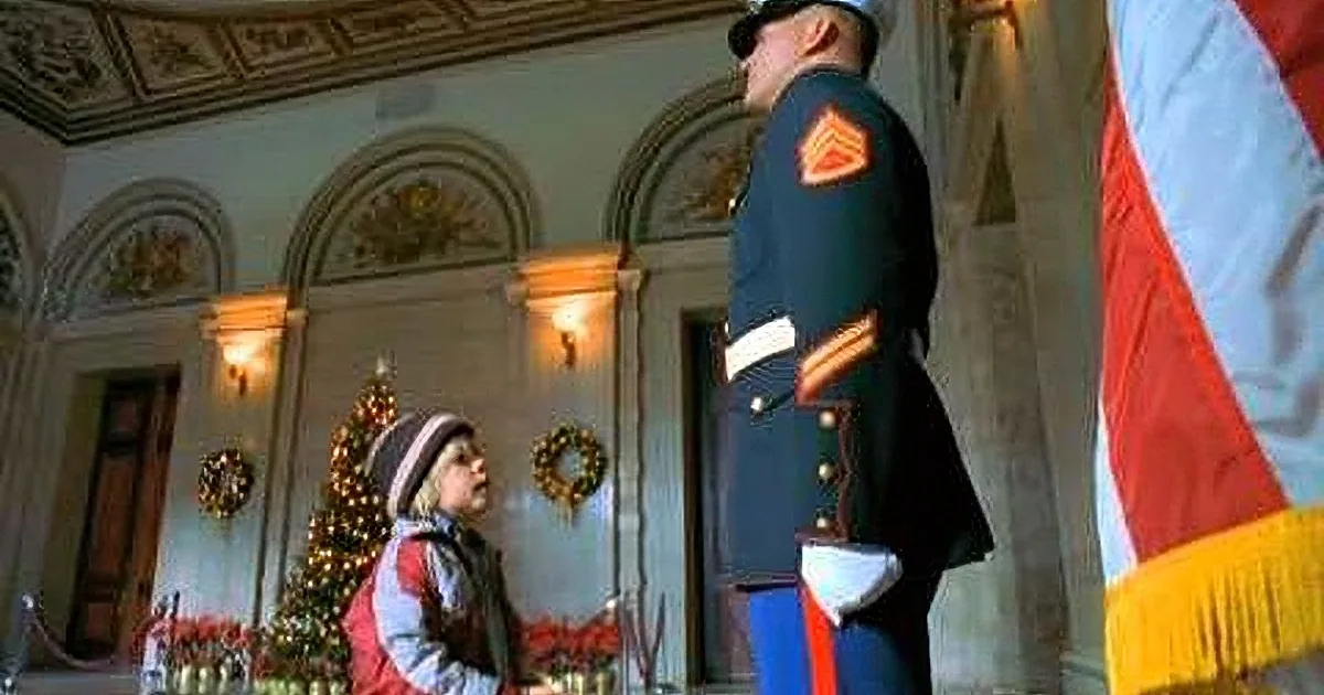 A young child in a red jacket stands before a uniformed officer in a decorated room with a Christmas tree.