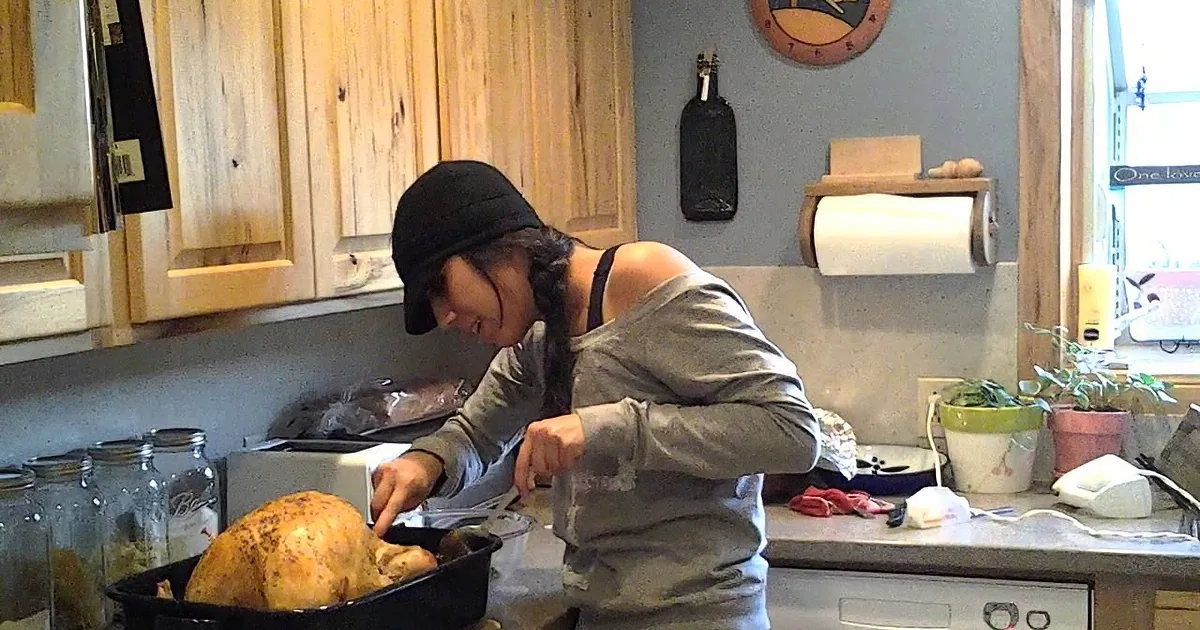 A person in a kitchen prepares a roasted turkey in a black pan on a counter.