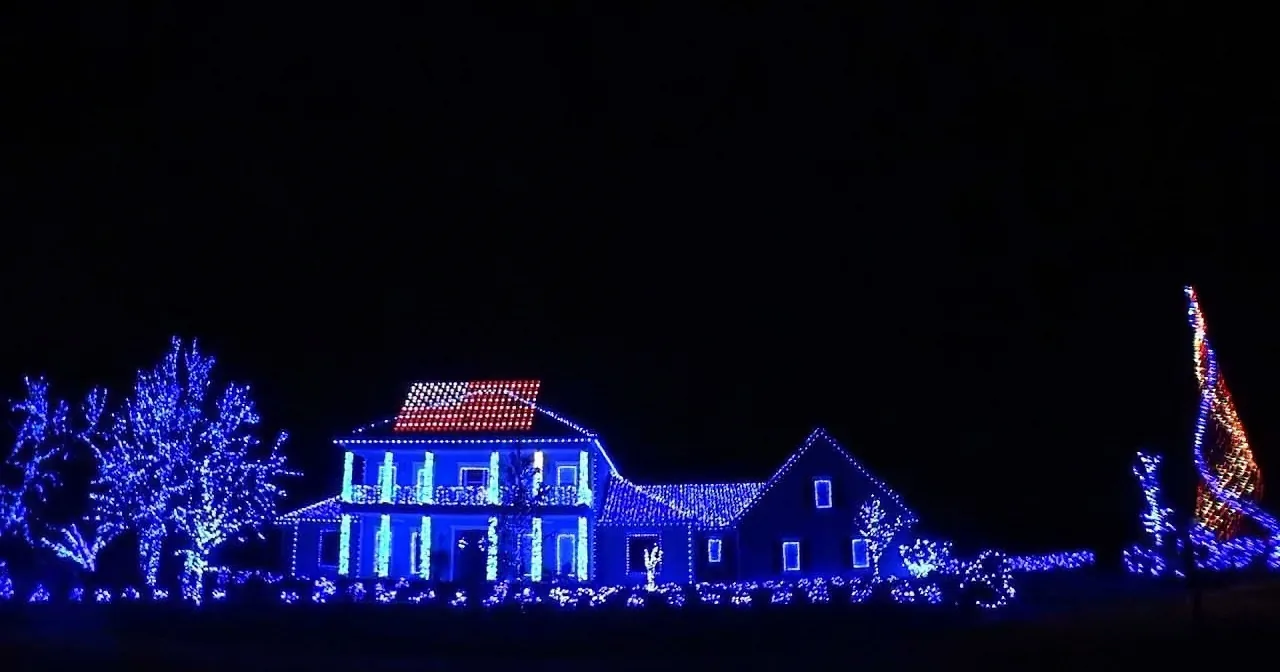 A house adorned with blue lights and festive decorations stands illuminated against a dark night sky.