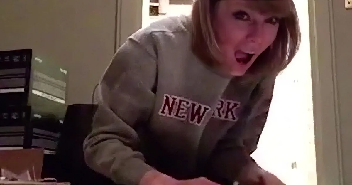 A person in a gray sweatshirt leans forward, holding something in their hands, with a surprised expression.