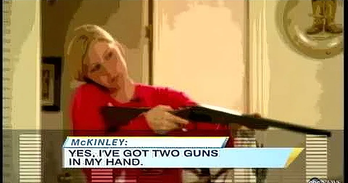 A woman in a red shirt holds a gun, with text on screen saying "Yes, I've got two in my hand."