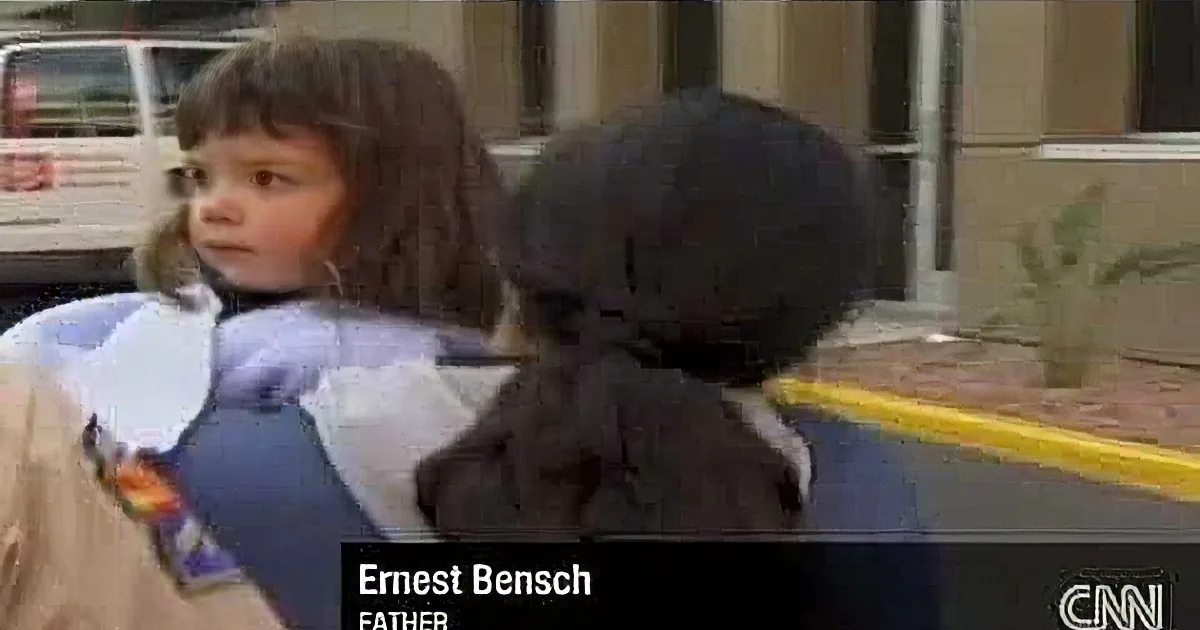 A young child is being held by a woman, with a man in the background.