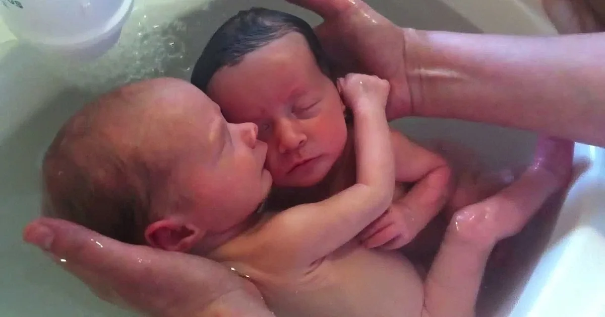 A newborn baby is being bathed in a tub, with hands supporting and washing the infant.