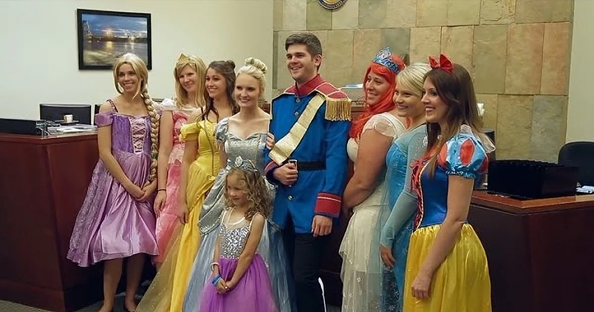 A group of people dressed as princesses and a prince pose together in an office setting.