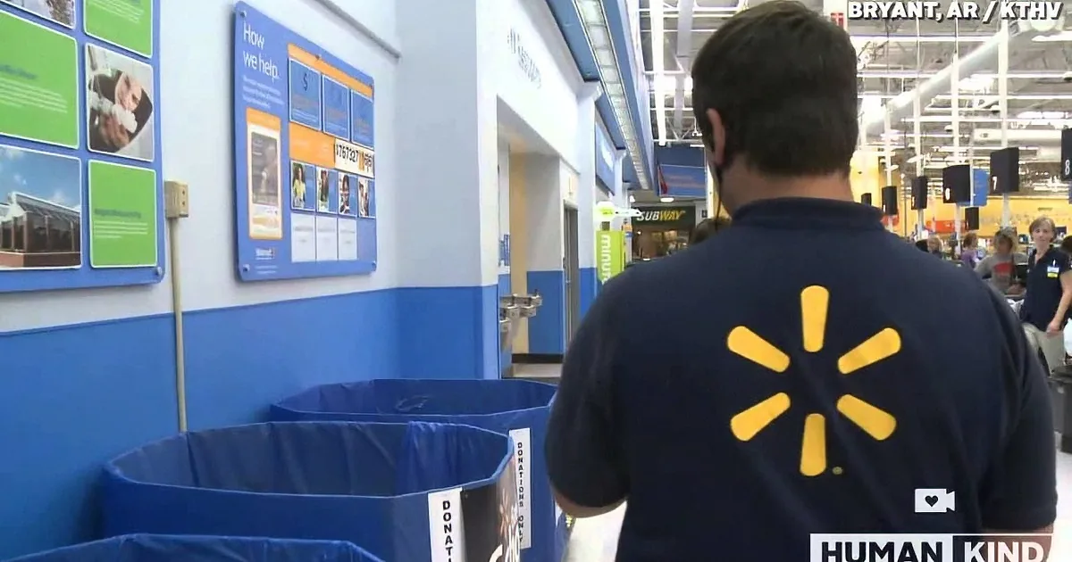 A Walmart employee in a blue shirt with the Walmart logo walks through a store aisle.
