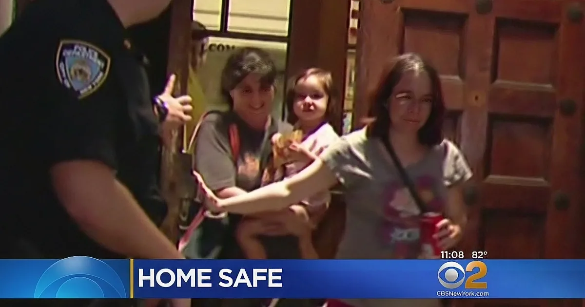 A woman holds a child as a police officer gives a thumbs-up, with "HOME SAFE" displayed on the screen.
