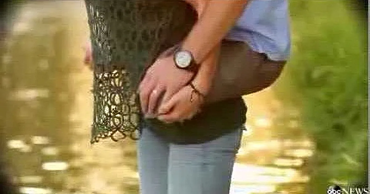 A person wearing a watch and holding a fish net, standing near water.