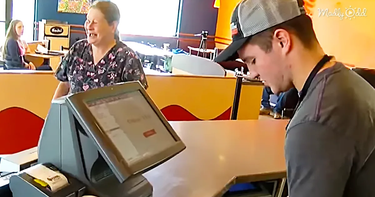 A cashier in a floral shirt laughs while a customer in a cap looks down at a computer screen in a brightly lit restaurant.