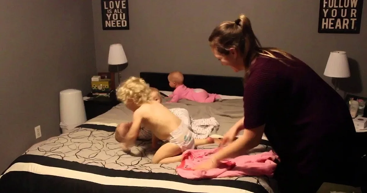 A woman helps a baby on a bed with two other children nearby, surrounded by framed quotes on the wall.