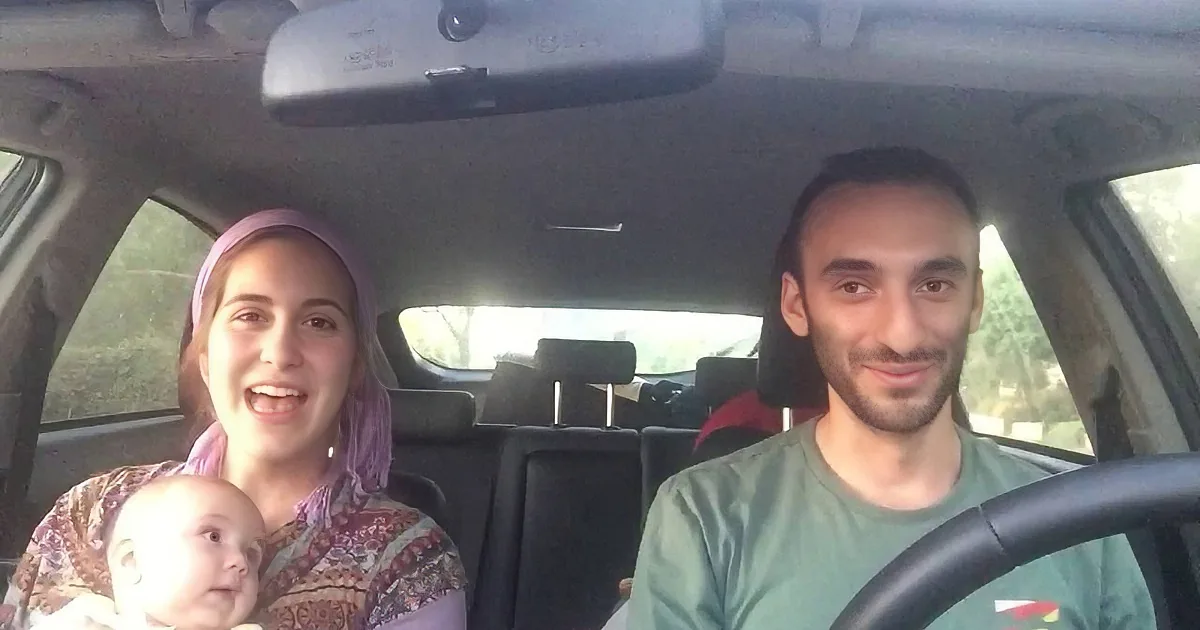 A man drives a car with a woman and a baby in the passenger seat.