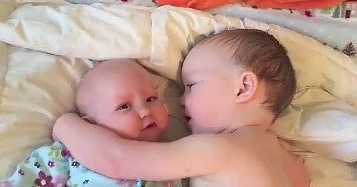Two babies are lying on a bed, one looking at the other, creating a tender moment.